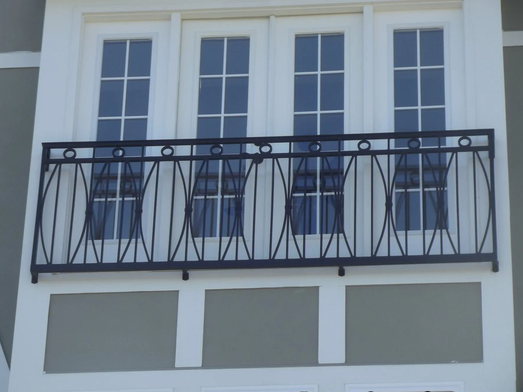 Black wrought iron balcony railing in front of three white-framed windows with blue curtains.