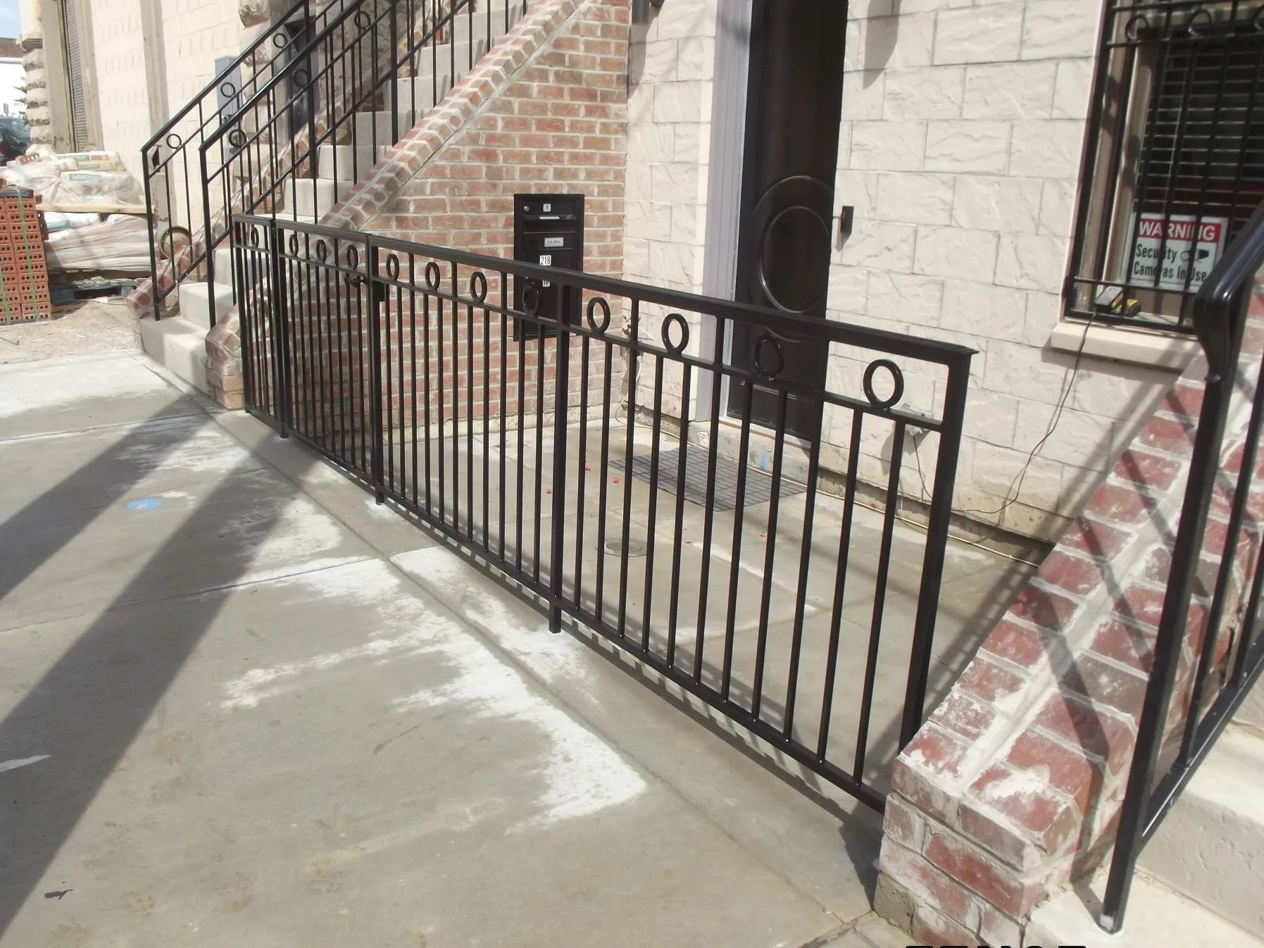 Black metal railing on a concrete porch, leading to building entrance. Brick and light-colored stone walls.