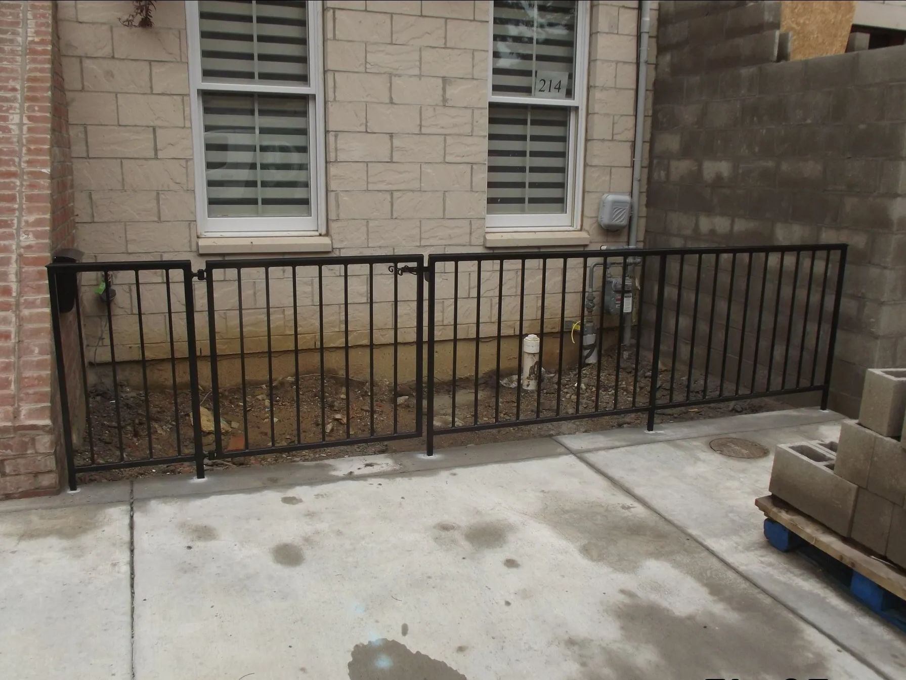 Black metal fence in front of a brick building with two windows.