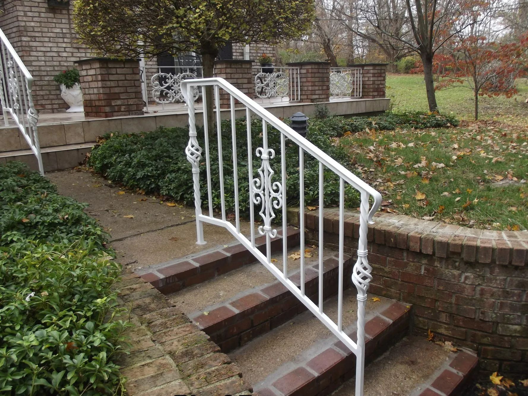 White wrought iron railing on brick steps leading to a house with a green lawn.