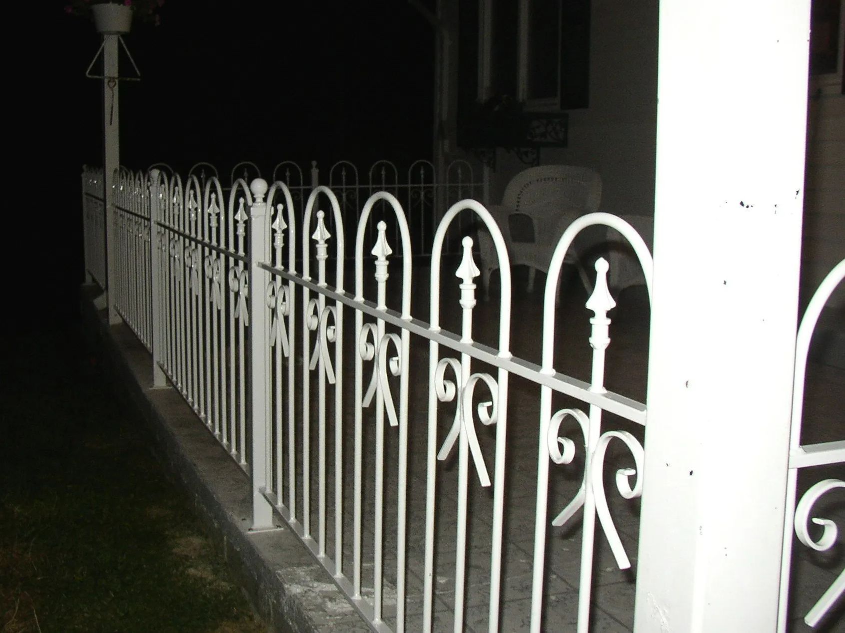 White decorative wrought iron fence on a porch at night.
