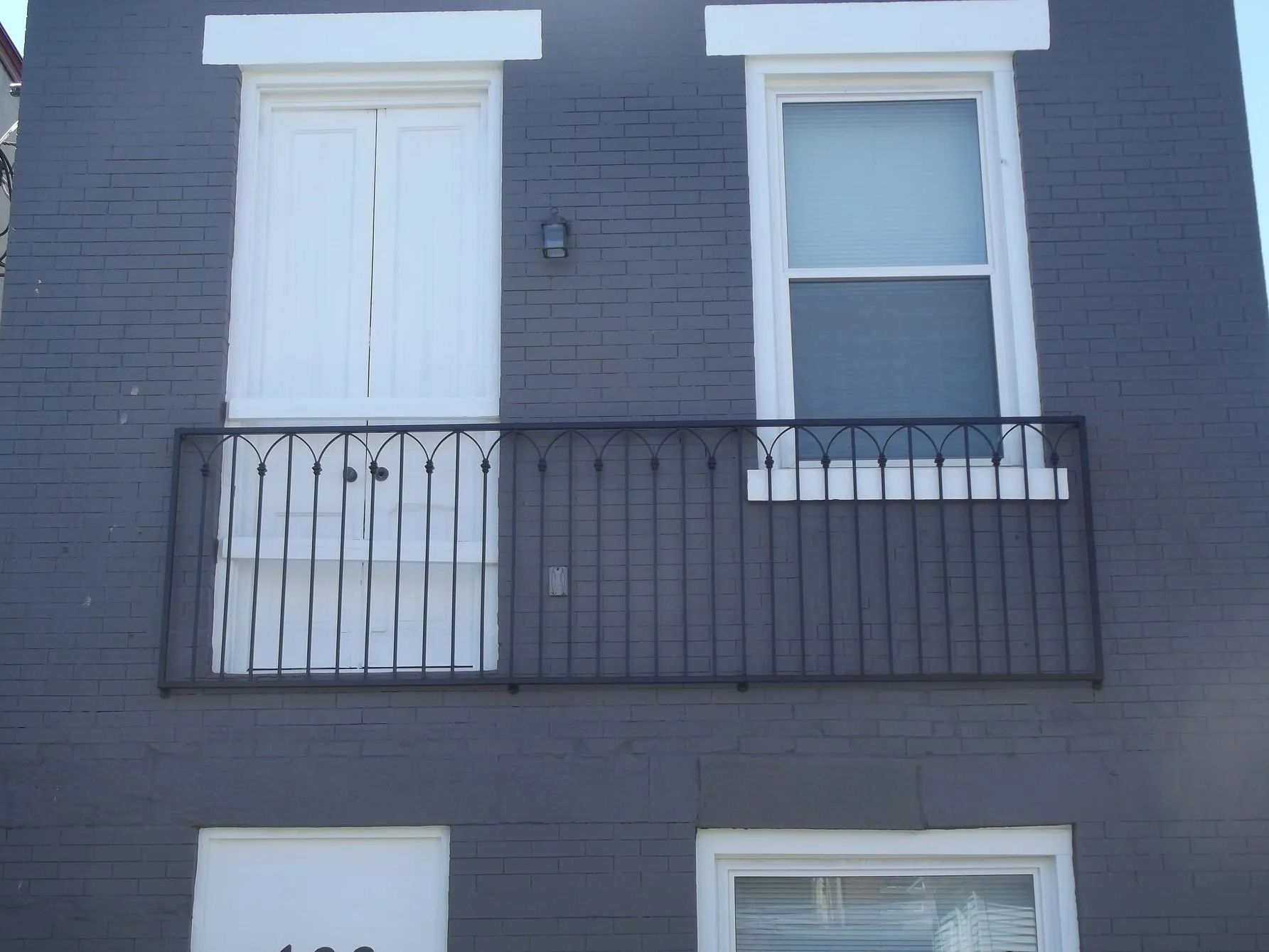 Gray brick building with white doors and a window above a decorative metal balcony.