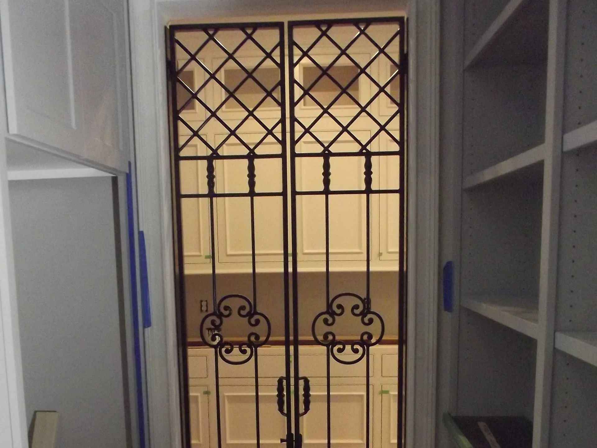 Black wrought iron doors in a white frame, leading into a room with white cabinets and shelves.