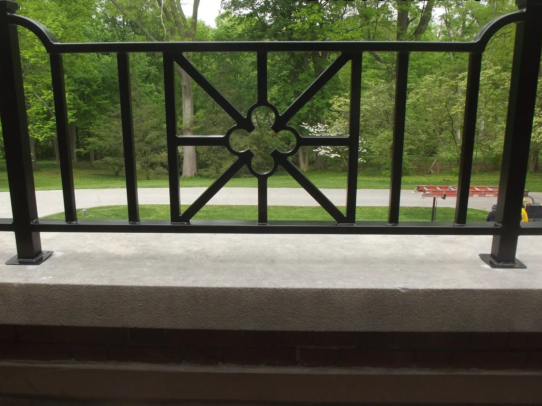 Black wrought-iron railing with a quatrefoil design, overlooking a green park with a pathway.