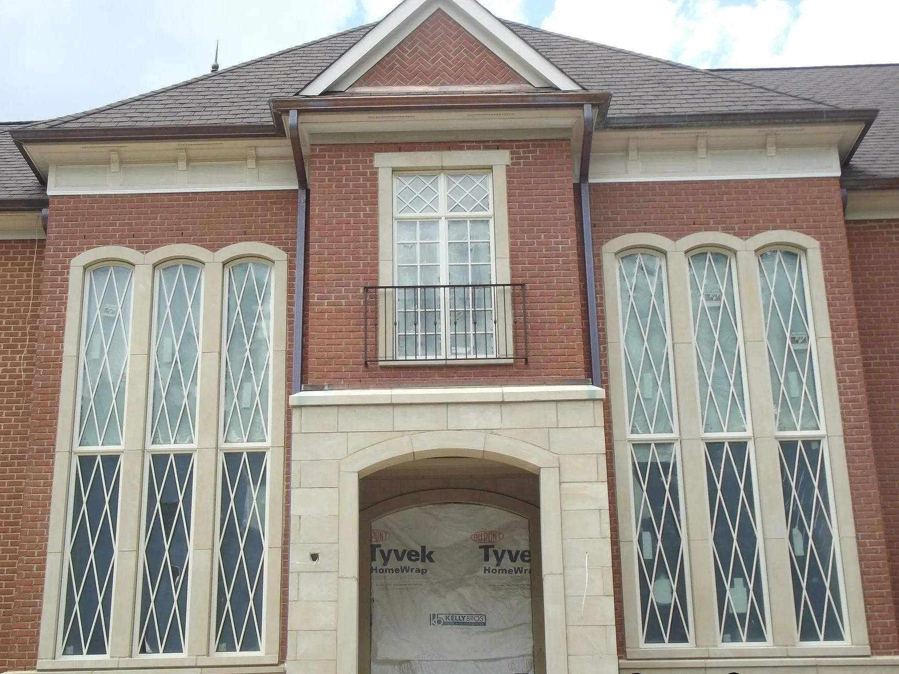 Brick building facade with tall windows, a balcony, and a stone entryway. Brown roof.