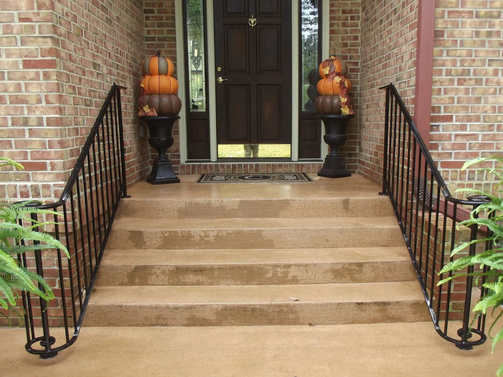 Brick home entrance with concrete steps and black iron railings, decorated with pumpkins.