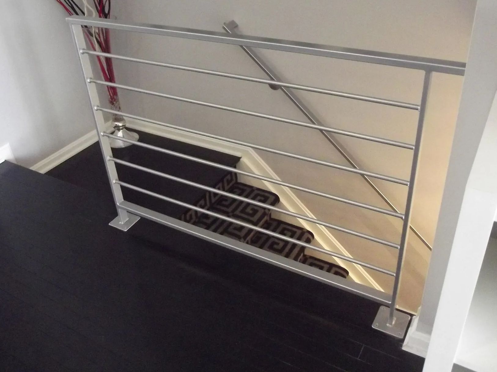 Modern metal stair railing. Horizontal bars, silver color. Dark wood floor and stair treads.