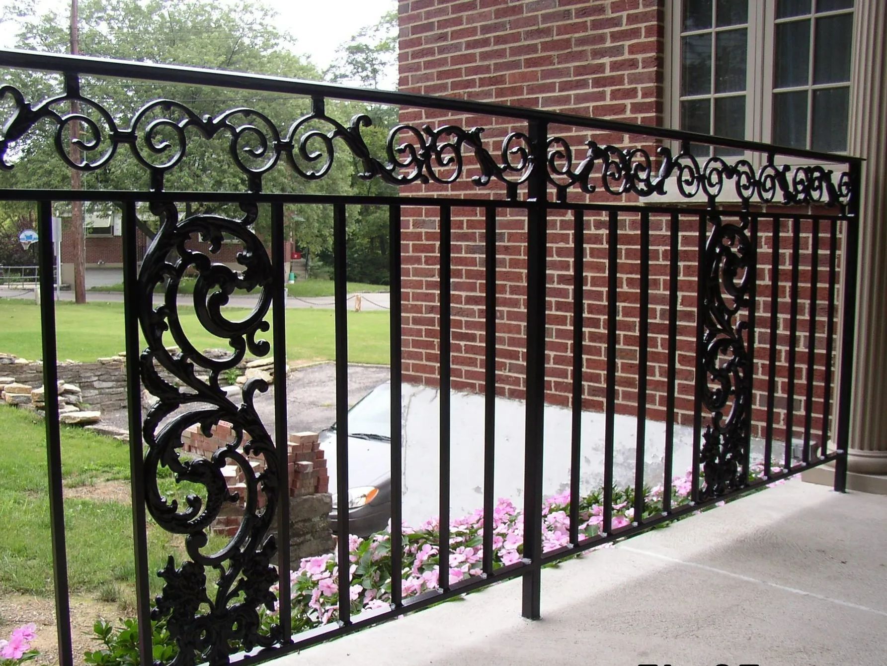 Black wrought-iron railing with decorative scrollwork on a brick building's porch.
