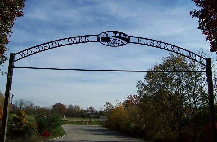 Wrought iron archway marking the entrance to Woodside Park in Elsmere, KY. Blue sky, fall foliage.