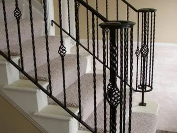 Black metal staircase railing with ornamental details, over carpeted stairs.