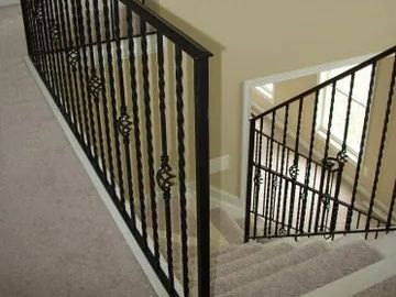 Black wrought iron staircase railing with decorative scrollwork on a beige carpeted landing and stairs.