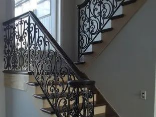 Ornate wrought iron railing on a wooden staircase. Black metal detailing, dark wood banister.