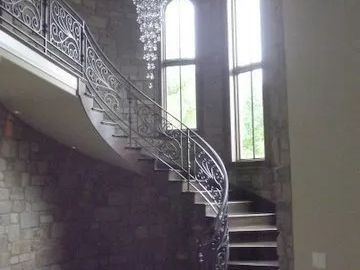 Curving staircase with ornate metal railing, stone walls, and large windows.