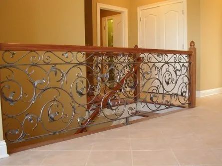 Ornate wrought-iron railing with wood top rail, tan walls, and a tiled floor.