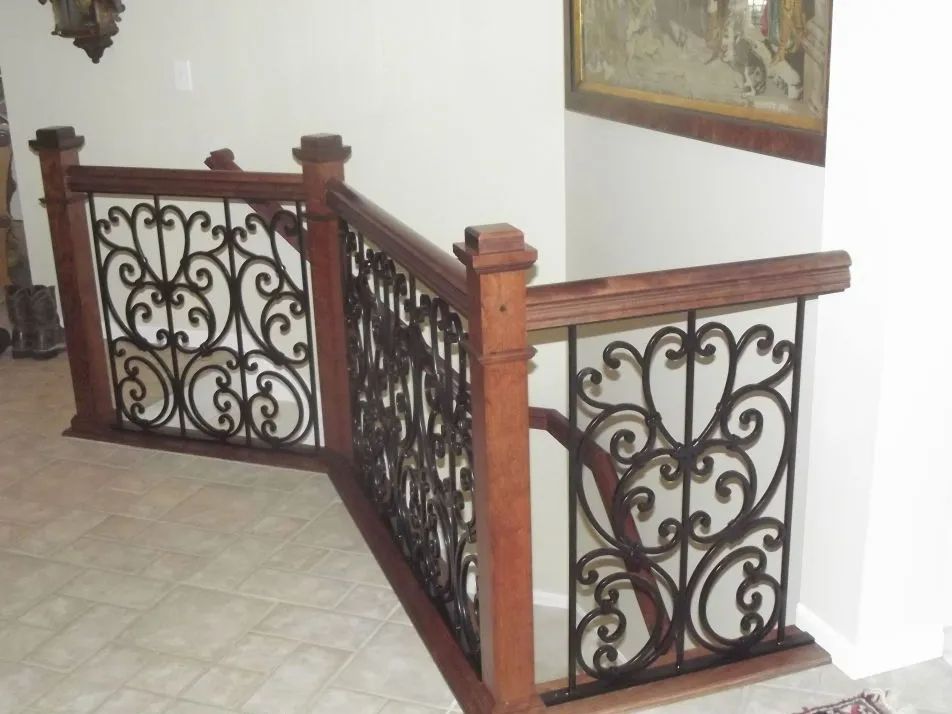 Wooden railing with ornate wrought iron panels, set in a tiled hallway.