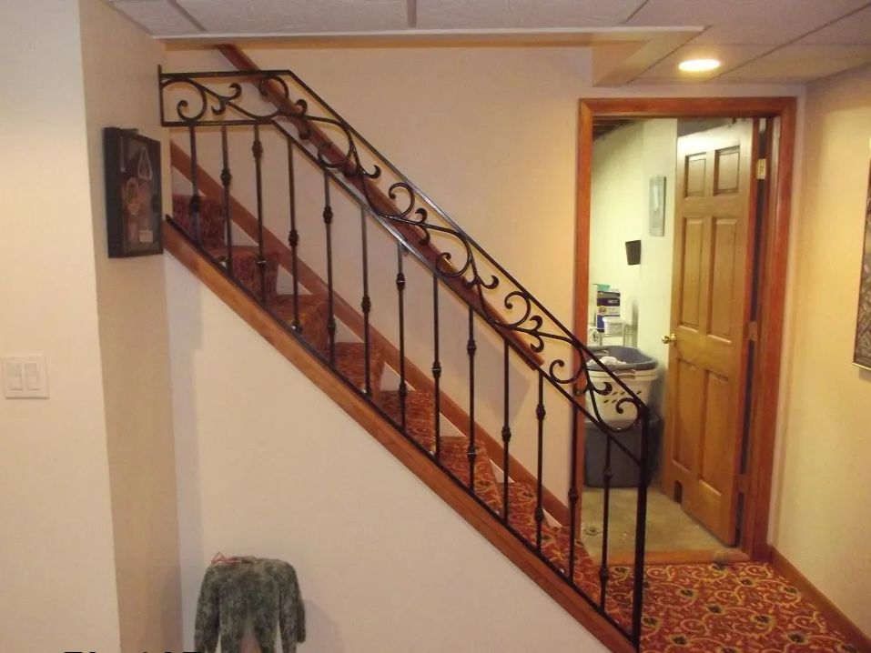 Staircase with iron railing, carpeted steps, and doorway leading to a room.