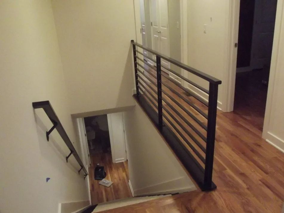 Interior view of a staircase with black horizontal railing and wooden floors.