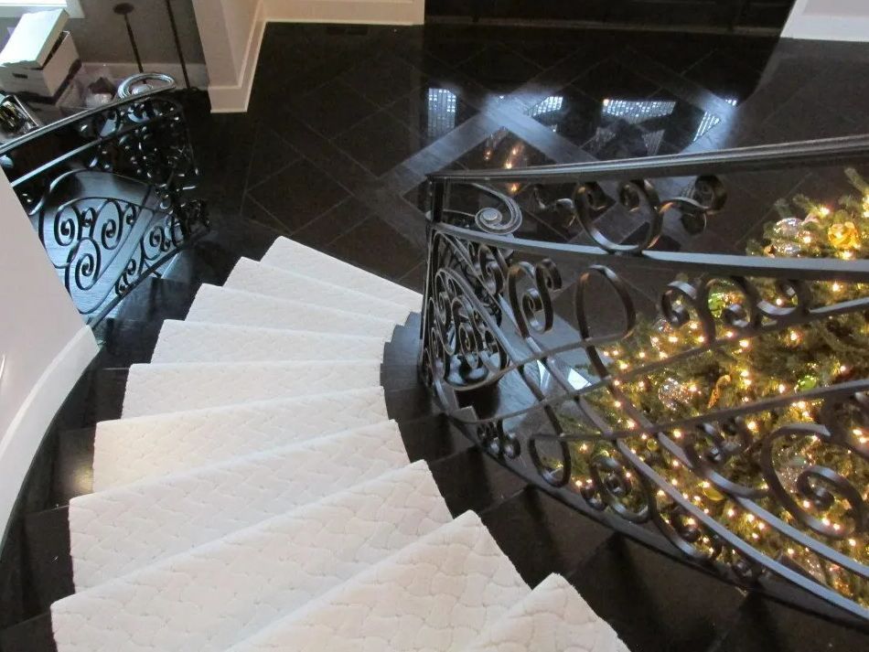 Curved staircase with white carpet and black tile, ornate wrought iron railing, Christmas tree visible.