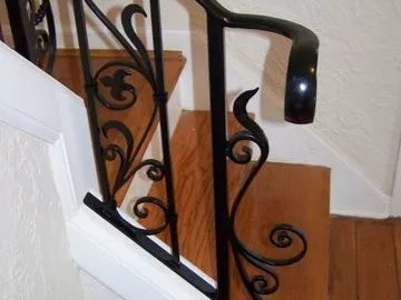 Black metal stair railing with ornate scrollwork on wooden stairs.