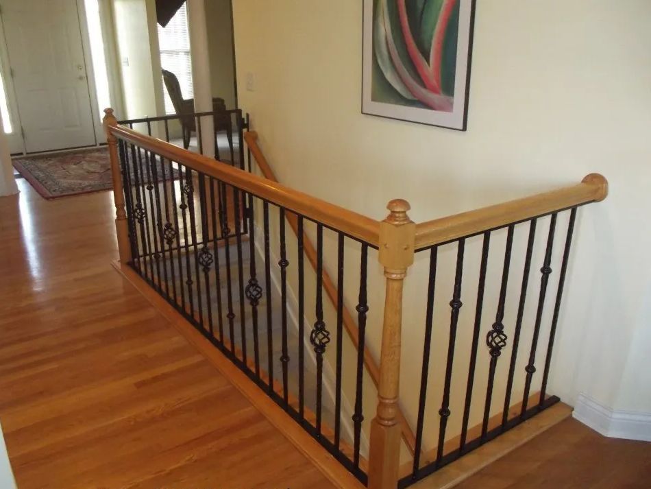 Wooden staircase railing with black iron spindles, light wood floor.