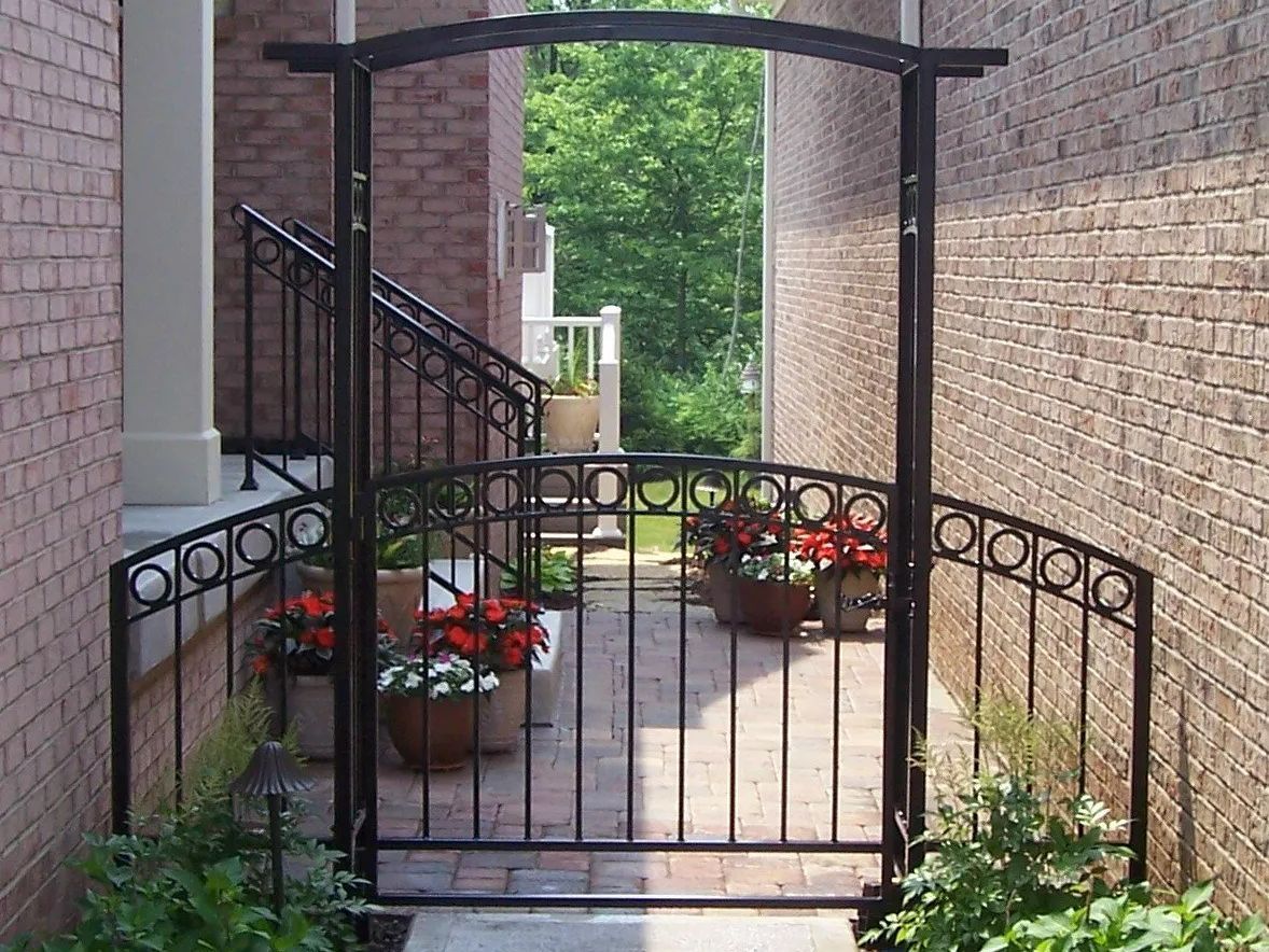 Black metal arched gate with matching railings, opening onto a brick path.