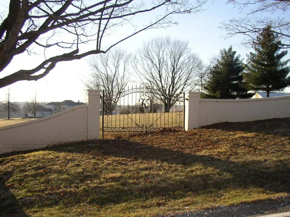 Stone wall with decorative gate in front of a yard and trees.