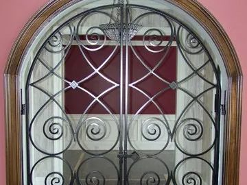 Ornate wrought-iron gate within an arched doorway, featuring swirling designs and a burgundy wall visible behind it.