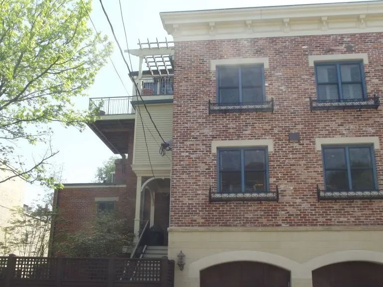 Brick building with dark-framed windows, two arched garage doors, and a deck with a pergola.