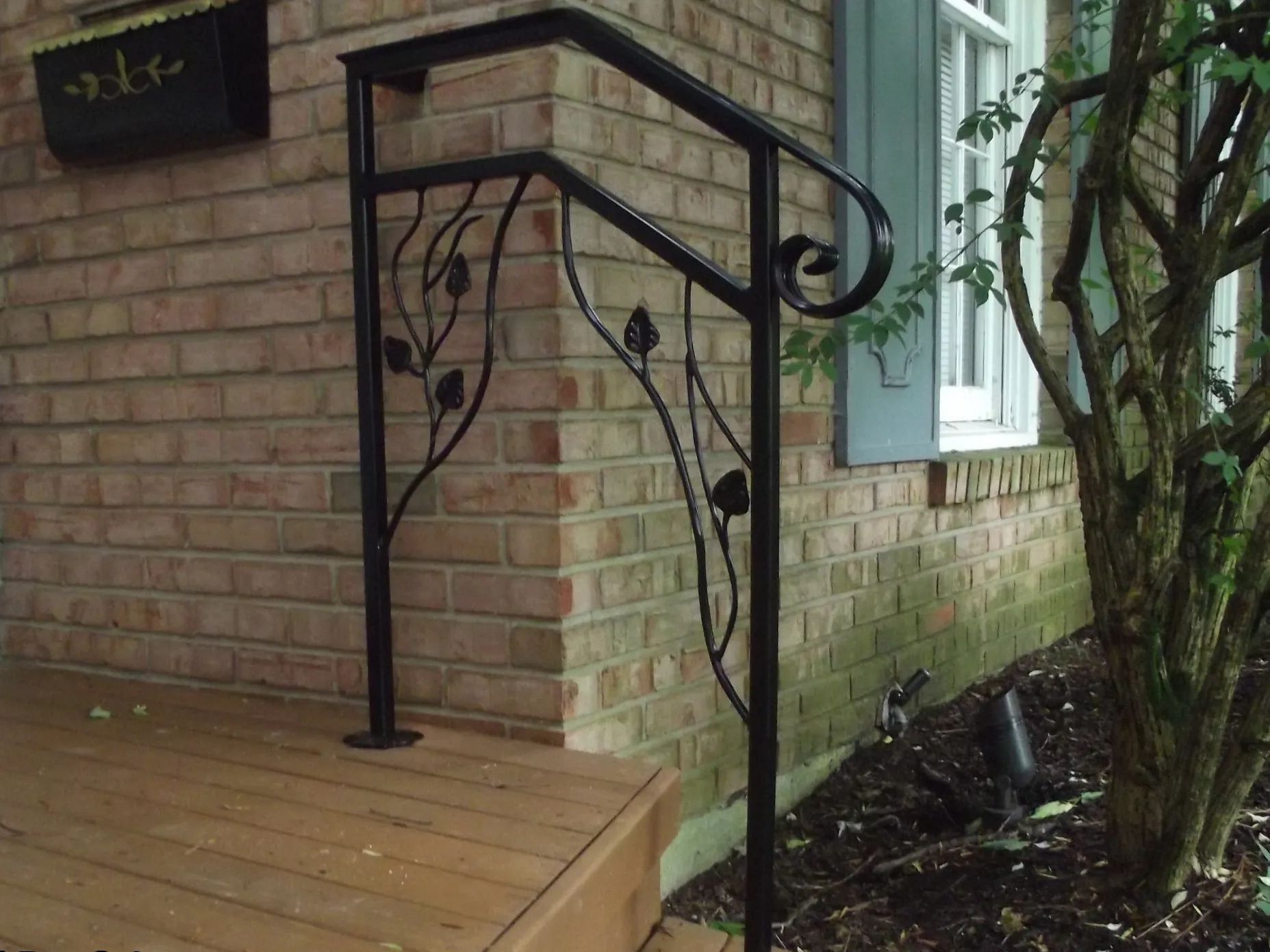 Black wrought-iron handrail on brick building's steps, with decorative leaves.