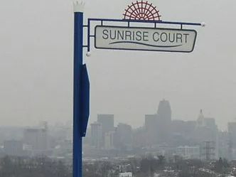 Sunrise Court street sign with cityscape in background. Blue and white sign, overcast day.
