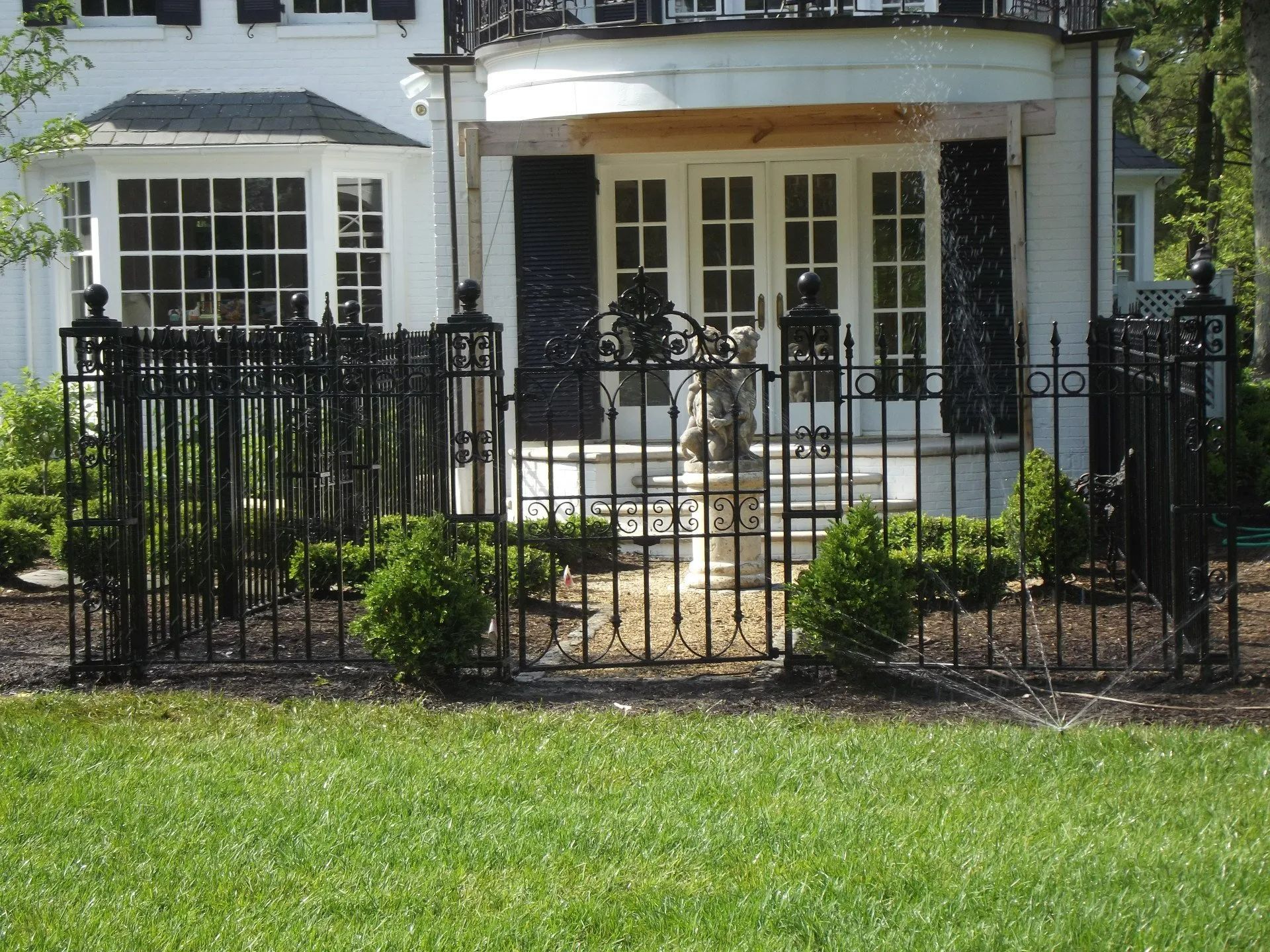 Black wrought iron fence surrounds a white house with double doors and a stone statue.
