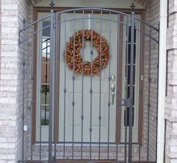 Metal security gate in front of a white door with a fall wreath. Brick wall and door frame.