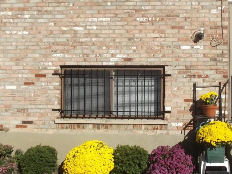 Brick building exterior with barred window and colorful potted mums in front.