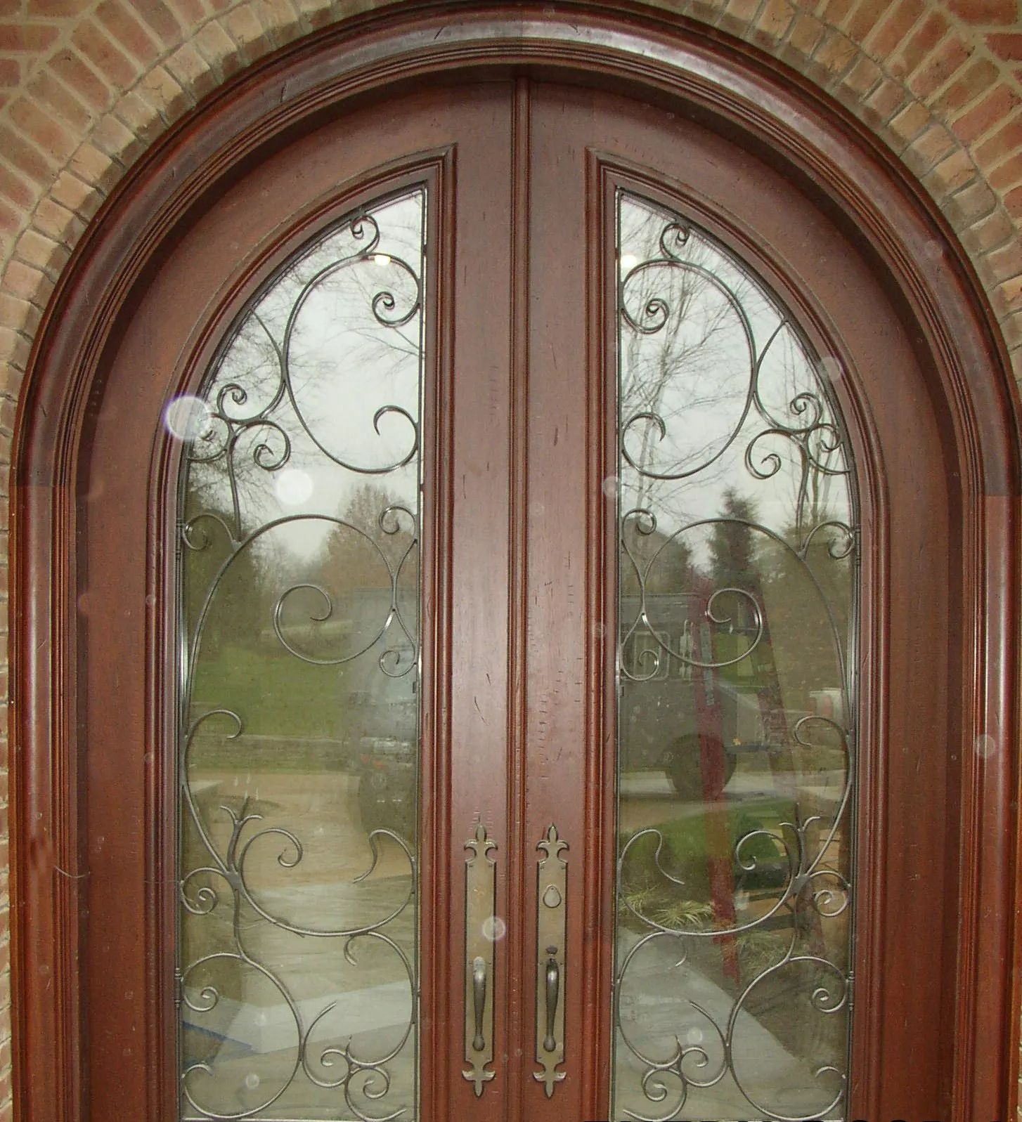 Wooden double doors with arched top, decorative ironwork, and glass panels.