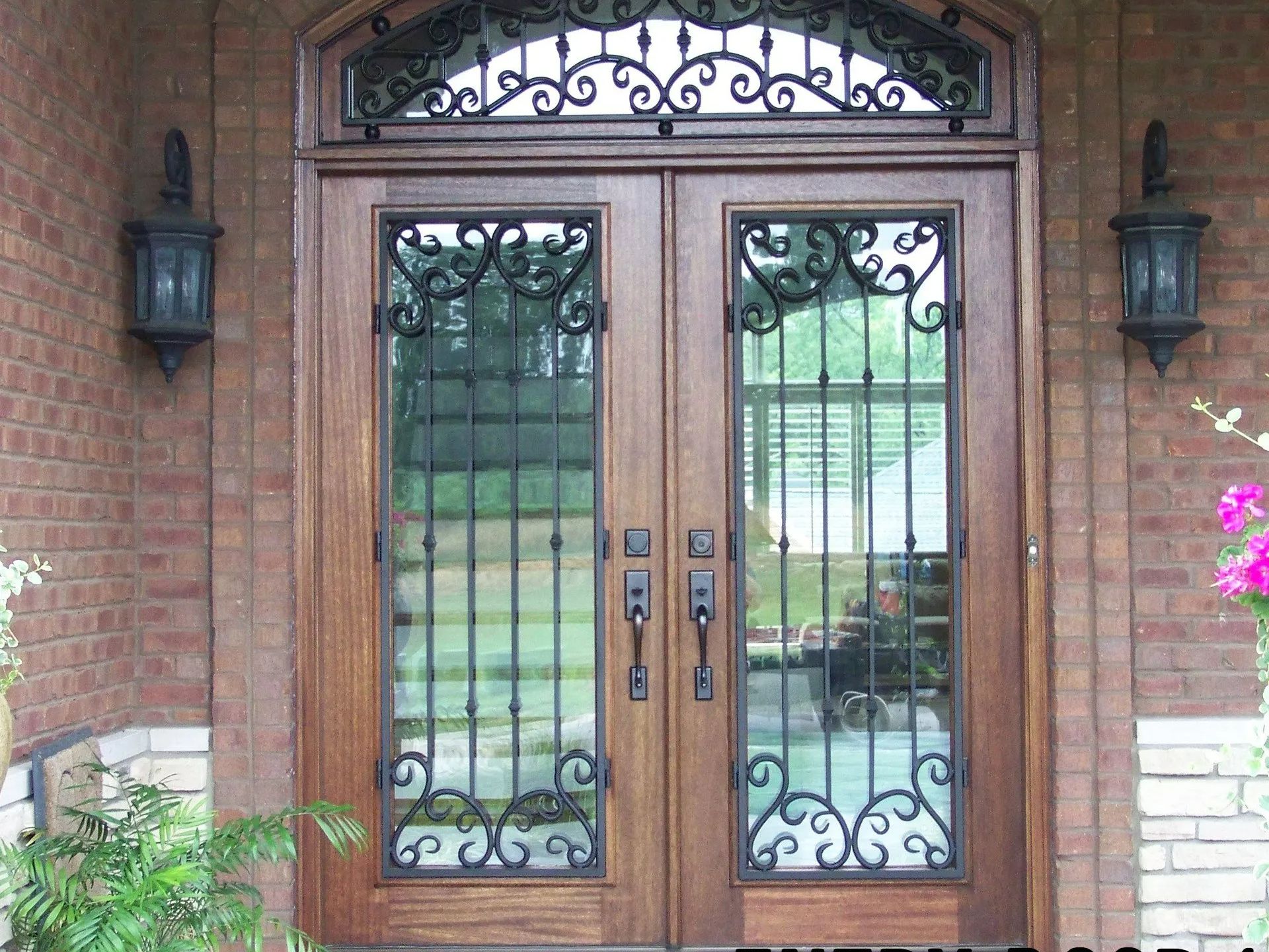 Double wooden front doors with decorative wrought iron and sidelights, flanked by brick, exterior.