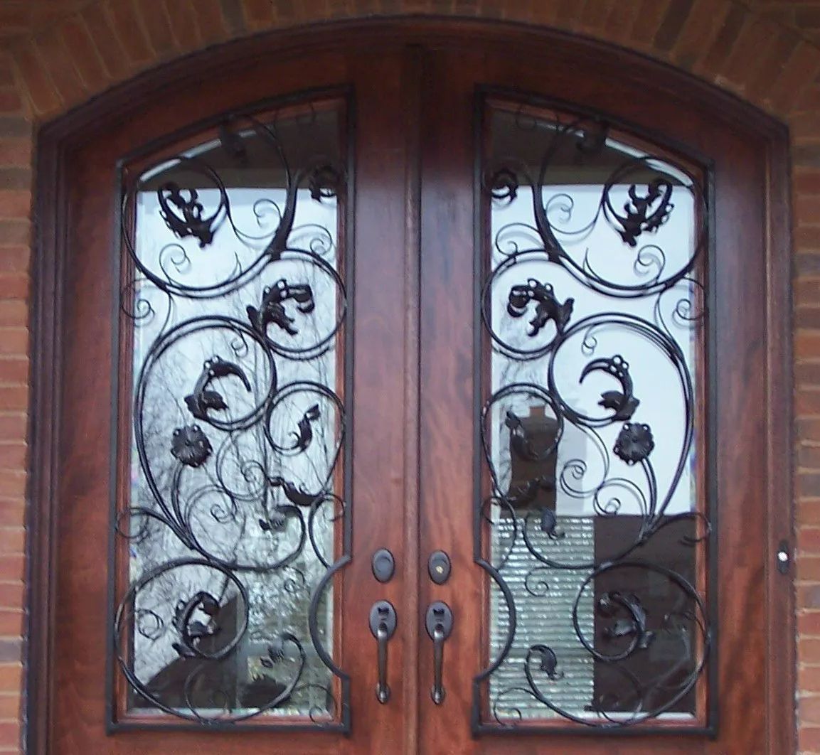 Double wooden doors with decorative wrought iron grilles and arched glass panes.