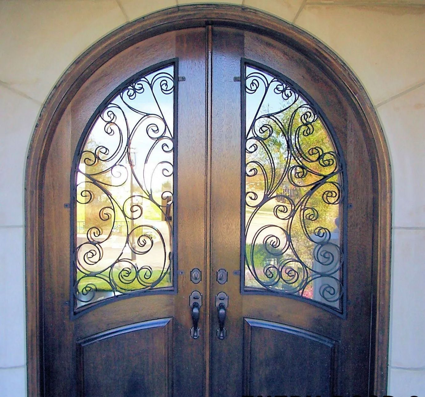 Wooden double doors with arched top, decorative ironwork, and clear glass panels.