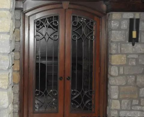 Wooden double doors with decorative wrought iron detail, set between stone walls.