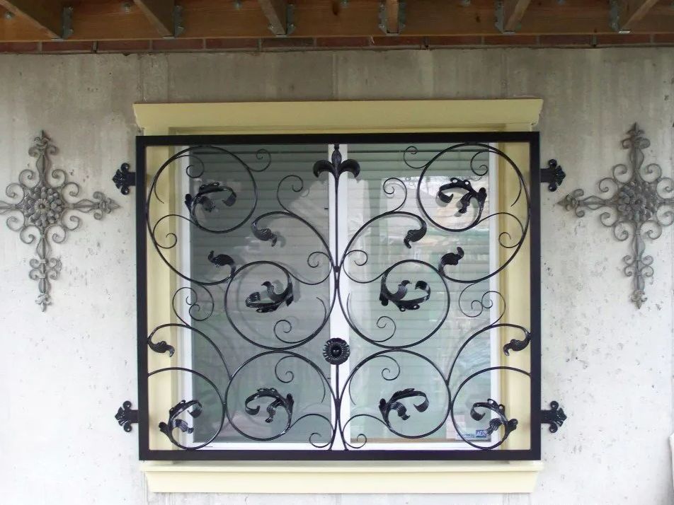 Window with black wrought iron security grille, decorative swirls, and flanking cross designs.