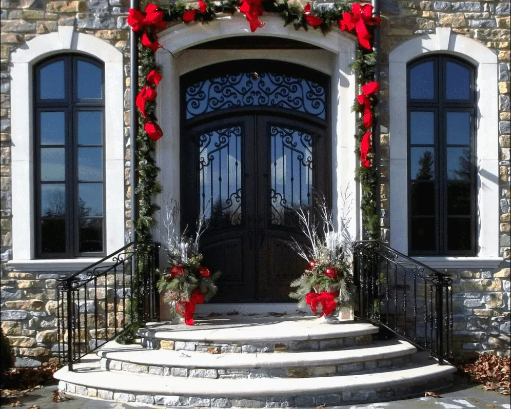 Festive entrance decorated for holidays with red bows and greenery. Stone steps lead to a dark double door.