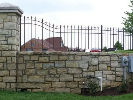 Stone wall with black metal fence on top; house in the background.