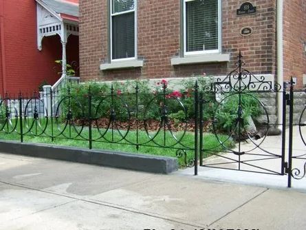 Black wrought-iron fence and gate in front of a brick house with a small garden.