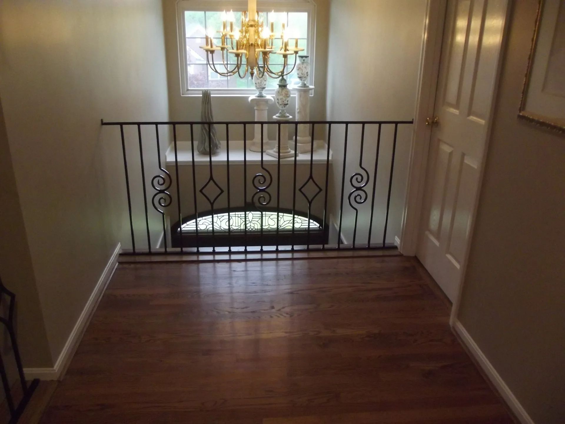 Hallway with hardwood floor, railing, window, chandelier, and decorative objects.