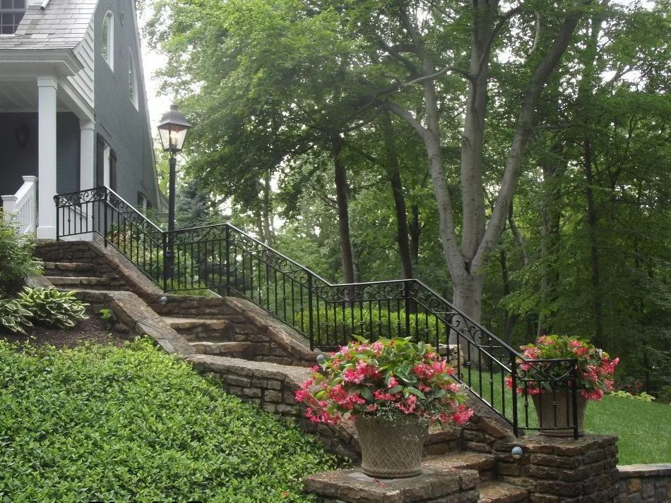 Stone steps with black railing lead to a house. Pink flowers in pots sit along the steps.