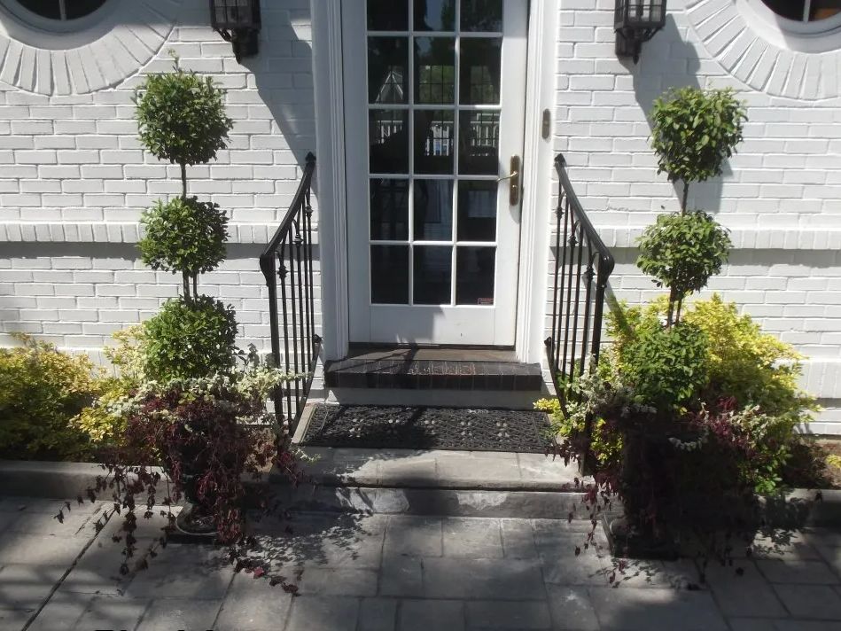 White brick facade with white door, black railing, and potted plants framing steps.
