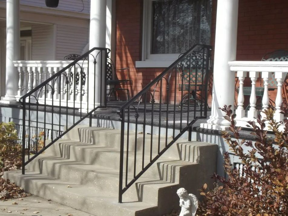Concrete steps with black metal railing leading up to a porch with white pillars.