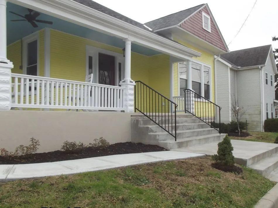 Yellow house with porch, black railings, and concrete steps.
