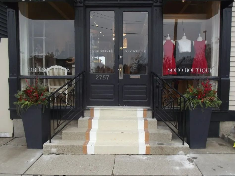 Storefront entrance with black door, steps, and railing. 