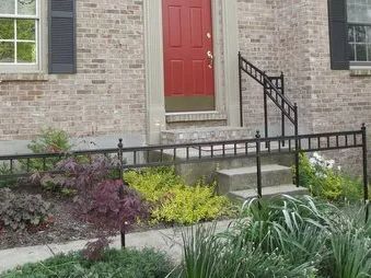 Brick house with red door, concrete steps, and black metal railings for accessibility.