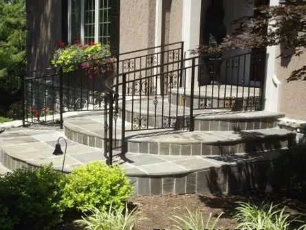 Stone steps leading to a house with black wrought iron railing and landscaping.